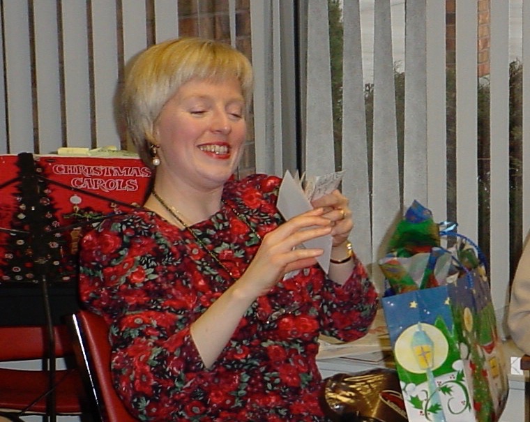 Helen smiles as she reads cards as she stands near Christmas gifts.